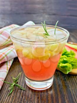 Lemonade with rhubarb and rosemary in a glass, the stems and leaves of rhubarb, a doily on a wooden boards background