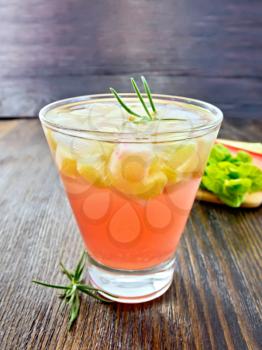 Lemonade with rhubarb and rosemary in a glass, the stems and leaves of rhubarb on a wooden boards background