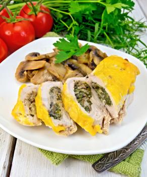 Roll of chicken breast with spinach, mushrooms and cheese in a white plate with grilled mushrooms and parsley on a napkin, tomatoes, dill, tarragon on a wooden boards background