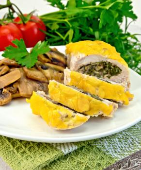 Roll of chicken breast with spinach, mushrooms and cheese in a white plate with grilled mushrooms and green parsley on a napkin, tomatoes, dill on a wooden boards background