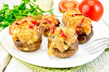Mushrooms stuffed with meat with parsley and tomatoes in a white towel on a plate, fork on the background light wooden boards
