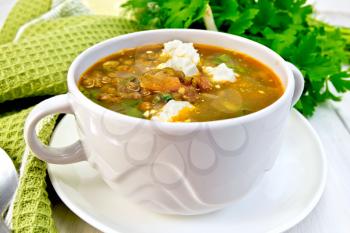 Lentil soup with spinach, tomatoes and feta cheese in a white bowl, spoon on a green napkin, parsley on the background light wooden boards