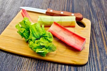Rhubarb stalks with green leaves and a knife on the planch on the background of wooden boards