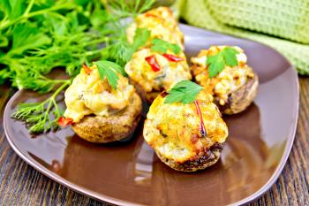 Mushrooms stuffed with meat with parsley and pepper in a brown plate green kitchen towel on the background of wooden boards