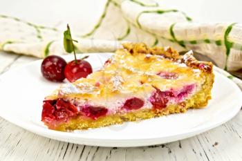 Pie with cherries and sour cream in a dish, towel on a background of wooden boards