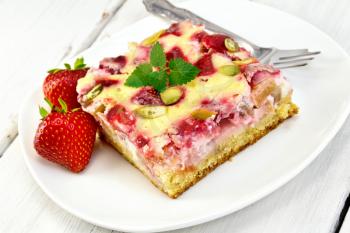 Piece of pie with strawberries, rhubarb and cream sauce, fork, strawberry, mint in white plate on a wooden boards background
