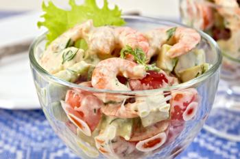 Salad with shrimp, avocado, tomato and mayonnaise, green lettuce in a glass goblet, a plate against the background of blue linen tablecloth