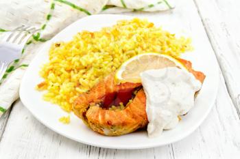Pink salmon with lemon, milk sauce and rice with turmeric in a dish, kitchen towel and fork on the background of wooden boards