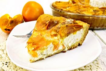 Sweet pie with curd and persimmons, a fork in the white plate on a napkin silicone, glass pan with pie on a wooden boards background
