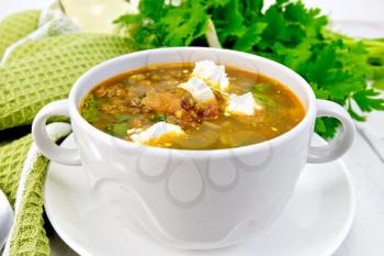 Lentil soup with spinach, tomatoes and feta cheese in a white bowl, spoon on a napkin, parsley on the background light wooden boards