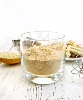 Sesame flour in a glass, a spoon with sesame seeds, cookie cutters and a mixer, biscuit on the background of wooden boards