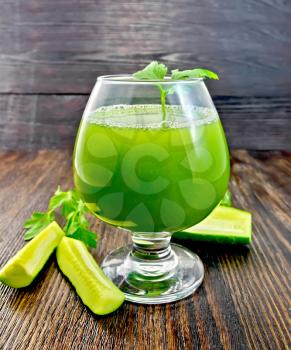 Cucumber juice in a wineglass, slices of cucumber and parsley on a wooden board background