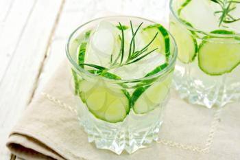 Lemonade with a cucumber and rosemary in two glassful on beige napkin against the backdrop of wooden planks