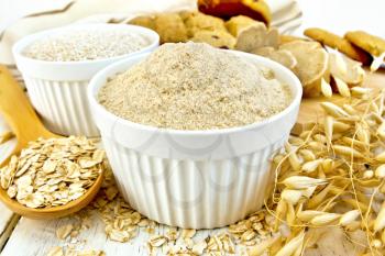 Flour and bran oats in white bowls, oat flakes in a spoon, stalks of oats, bread and biscuits, napkin on a background of wooden boards