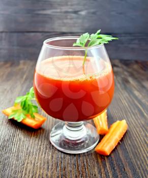 Carrot juice in a wineglass, carrots and parsley on a wooden boards background