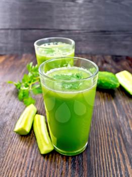 Cucumber juice in two tall glasses, cucumber and parsley on a wooden board background