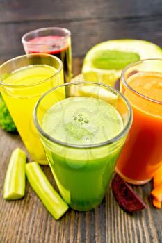 Four tall glasses with the juice of carrot, cucumber, beetroot and pumpkin with vegetables on the background of wooden boards