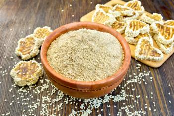 Sesame flour in a clay bowl and homemade cookies on a wooden boards background