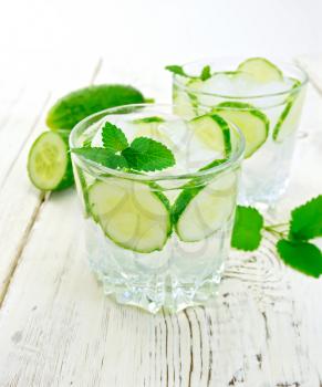 Lemonade with cucumber and mint in two glassful, sliced cucumber on a wooden boards background