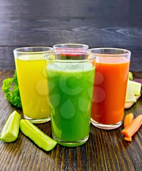 Four tall glasses with the juice of carrot, cucumber, beetroot and pumpkin with vegetables on the background of dark wood planks