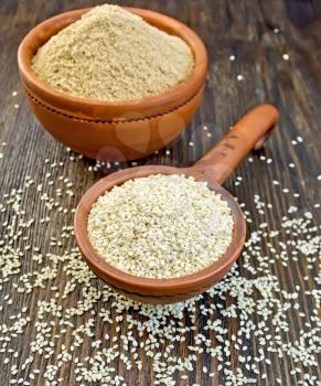 Sesame seeds in a clay ladle and sesame flour in a bowl on a wooden boards background
