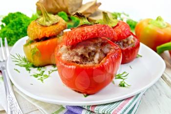 Sweet pepper stuffed with meat and rice in a plate on a napkin, fork, dill and parsley on a wooden boards background