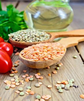 Lentils red and green in two wooden spoons, tomatoes, parsley, vegetable oil in a decanter on a wooden boards background