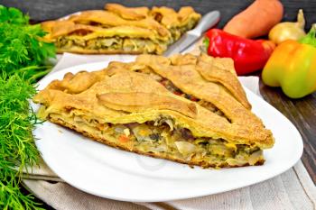 Pie with cabbage, sorrel and sweet peppers in a white plate on a napkin, parsley and vegetables on the background of wooden boards