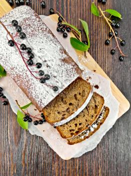 Fruitcake bird cherry cut with berries on a paper on the background of the wooden planks top
