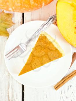 A piece of pumpkin pie in a white plate, pumpkin on the background light wooden boards on top