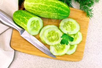 Cucumbers cut with parsley and a knife on a wooden board, cloth and dill on the background of a granite table top