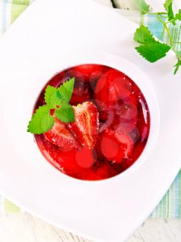 Strawberry jelly with mint and berries in white plate on the kitchen towel on a background of wooden boards on top