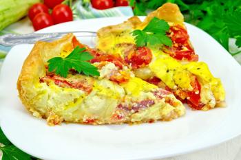 Two pieces pie of zucchini with tomatoes and eggs in a white plate on a napkin, parsley on a wooden boards background