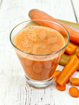 Carrot juice in a tall glass, vegetables on the background of wooden boards
