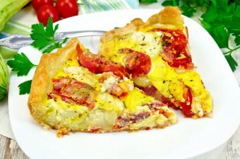 Two pieces pie of zucchini with tomatoes and eggs in a plate on a napkin, parsley on a wooden boards background