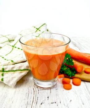 Carrot juice in a tall glass, vegetables with parsley, napkin against the background of wooden boards