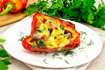Sweet pepper stuffed with sausage, egg and cheese with dill in white plate on a napkin, parsley on the background of the stone table