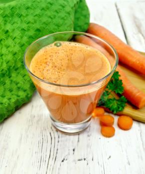 Carrot juice in a tall glass, vegetables, parsley, green cloth on a background of wooden boards