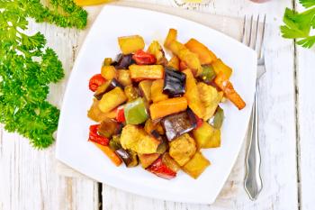 Roast meat, zucchini, eggplant, carrot and sweet pepper with honey, soy sauce and red wine in a plate on a napkin against the background of the wooden planks on top