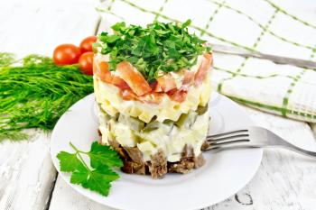 Salad with beef, boiled potatoes, pickles, cheese, tomato, parsley in the plate, napkin, dill on the background light wooden boards