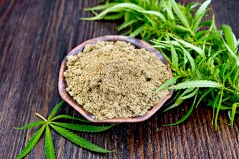 Hemp flour in a bowl, cannabis leaves on the background of wooden boards