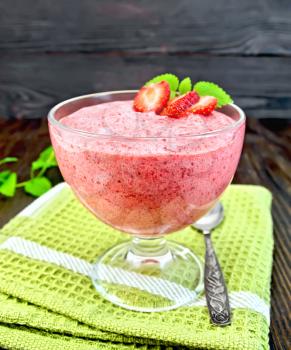 Jelly air strawberry in a glass bowl, a spoon on a green towel, mint on the background of wooden boards