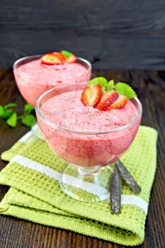 Jelly strawberry air in two glass bowls, spoons on green towel, mint on the background of wooden boards