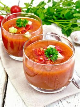 Gazpacho tomato soup in two glasses with parsley and vegetables on a napkin on the background light wooden boards
