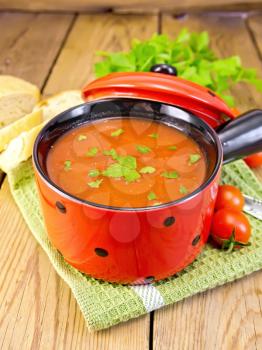 Tomato soup in a red bowl on a green napkin, tomatoes, bread, parsley on a wooden boards background