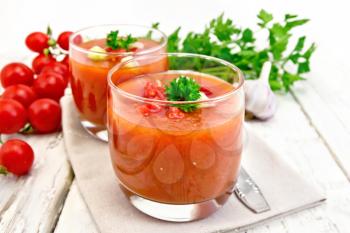 Gazpacho tomato soup in two glasses with parsley and vegetables on a napkin against the background of wooden boards