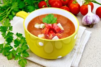 Gazpacho tomato soup in yellow bowl with parsley and vegetables on a towel on the background of the stone table
