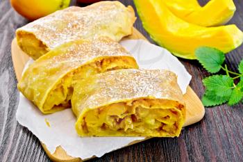 Strudel pumpkin and apple with raisins on paper, fruits and vegetables on a dark wooden board