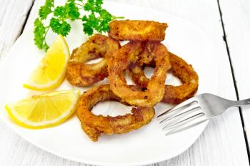 Breaded fried squid rings on a plate with slices of lemon and parsley on the background light wooden boards