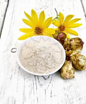 Flour of Jerusalem artichoke in a bowl with flowers and vegetables on the background light wooden boards